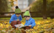 Two boys, reading a book on a lawn in the afternoon