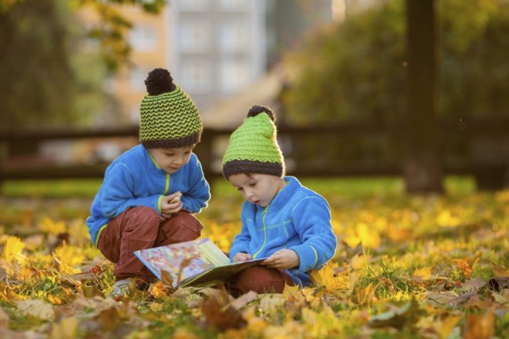 Two boys, reading a book on a lawn in the afternoon